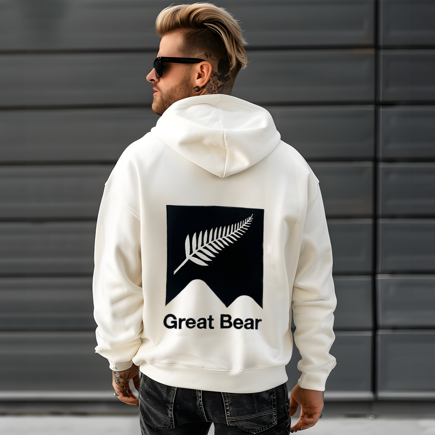 New Zealand man wears luxury oversized off white hoodie with image of the Great Bear logo and the New Zealand black background with white fern embroidered onto the back