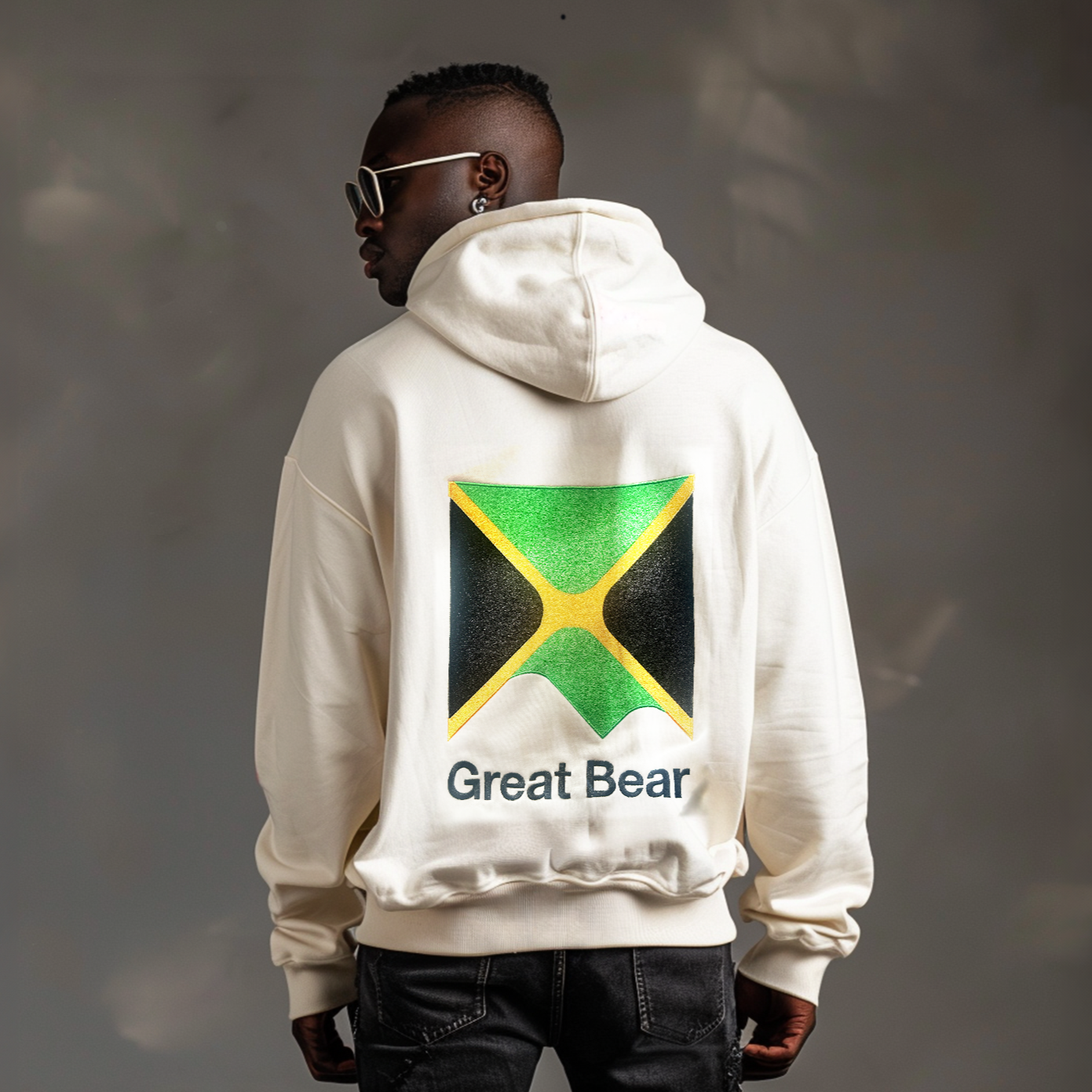 Jamaican man wears luxury oversized off white hoodie with image of the Great Bear logo and the Jamaica yellow green and black flag embroidered onto the back